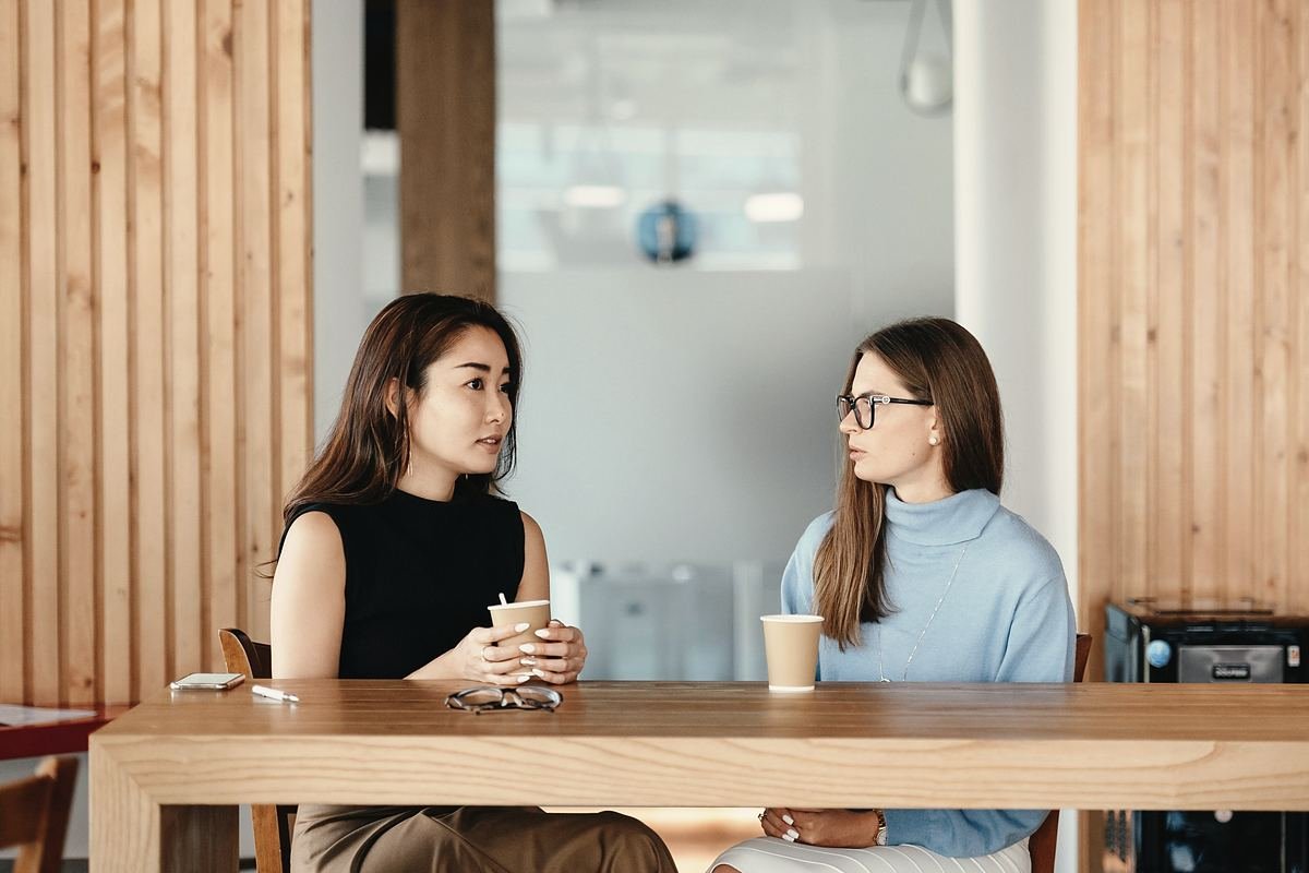 Two people in conversation across a light wooden table