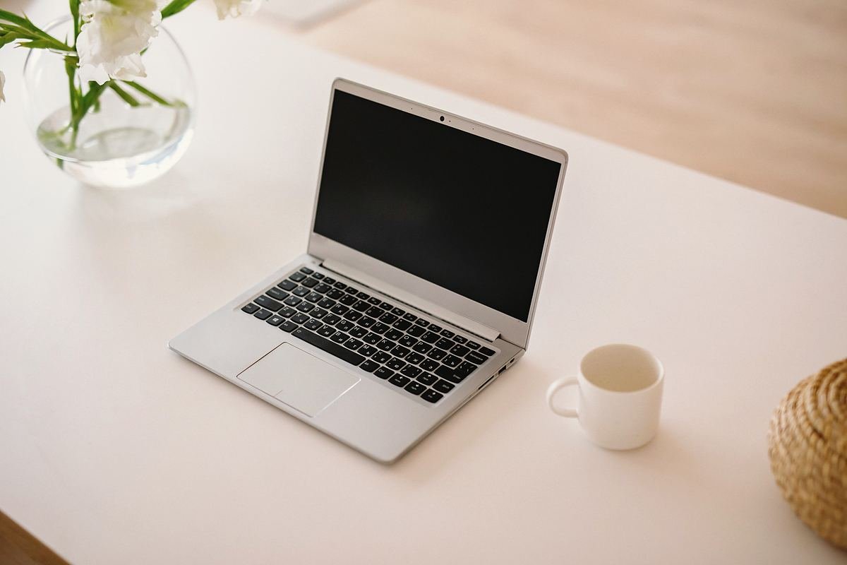 A laptop and a cup on a pale desk in soft daylight